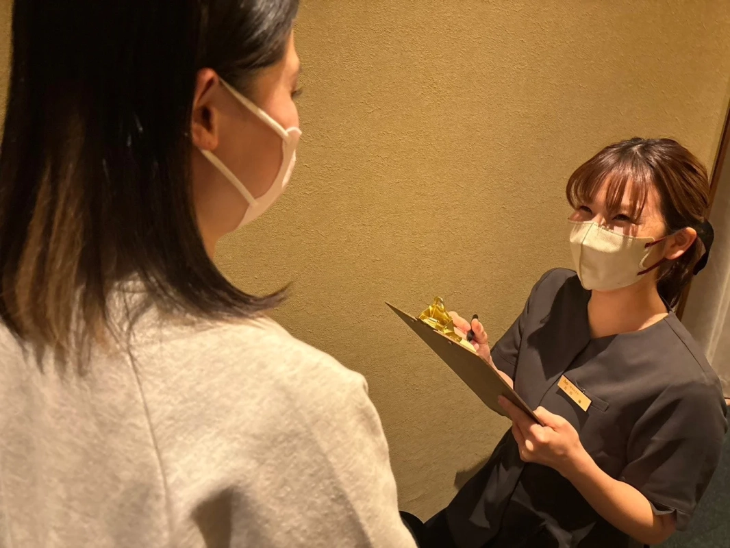 マスクを着用した女性スタッフが、問診票を手に顧客と対話している場面