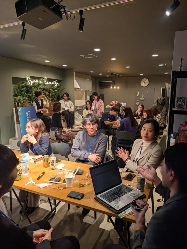 モダンなラウンジで、人々がテーブルを囲み、飲み物や軽食を楽しみながら交流している