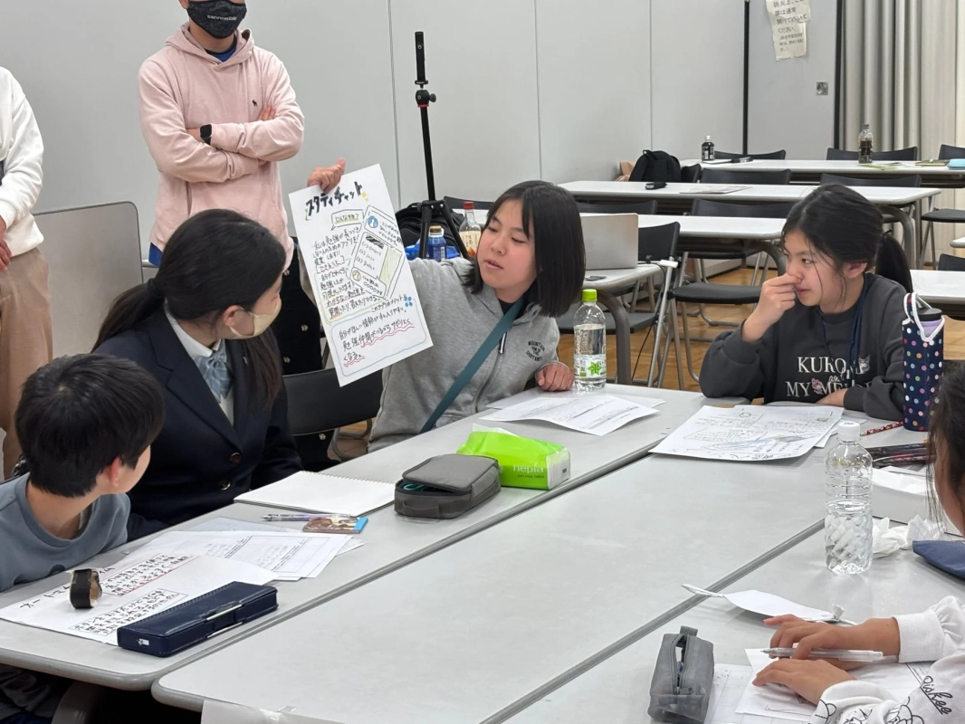 スタディチャットと書かれた資料を手にプレゼンテーションを行っている少女