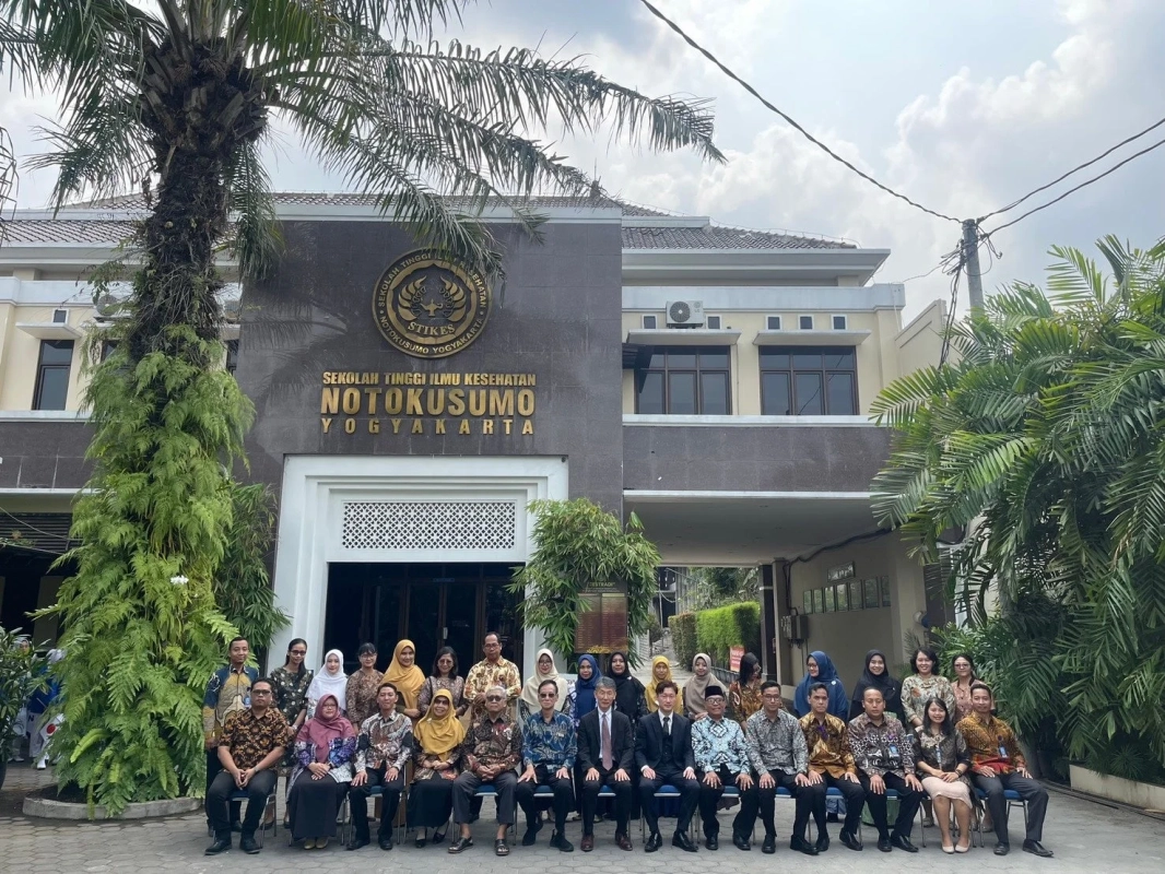 インドネシアのジョグジャカルタにあるノトクスモ健康科学大学の前で、教職員と思われる人々が集合写真を撮っています。