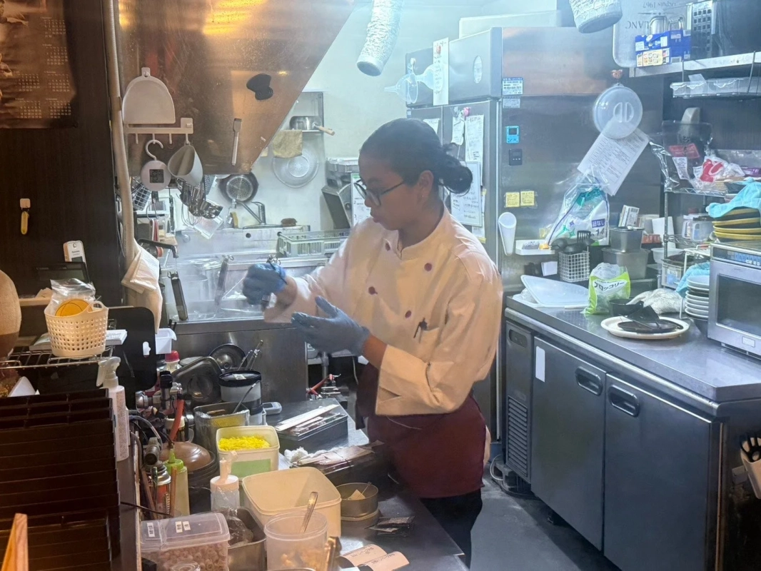 プロの厨房で、コックコートと手袋を着用した人物が忙しく調理作業を行っています。