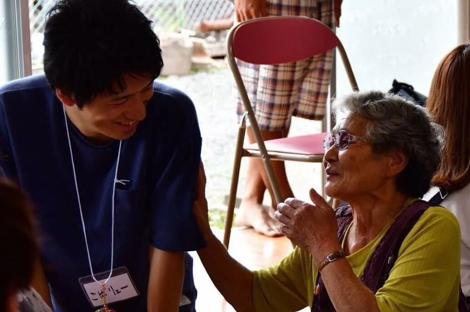 笑顔の若い男性が、身振り手振りを交えながら話す高齢の女性と温かい会話をしています。