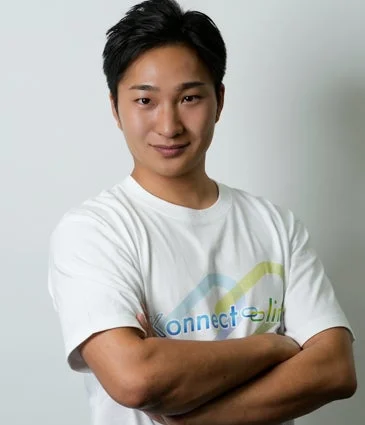 白いTシャツを着た若い男性が、腕を組み笑顔でカメラを見つめているポートレート写真