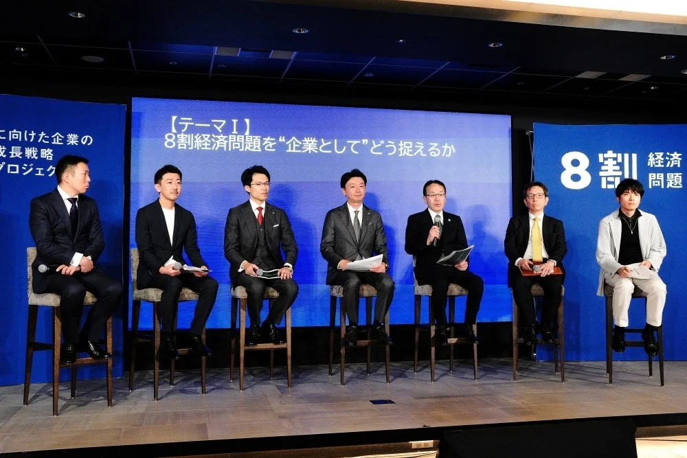 ビジネスイベントで7人の男性がステージ上でパネルディスカッションを行っている様子