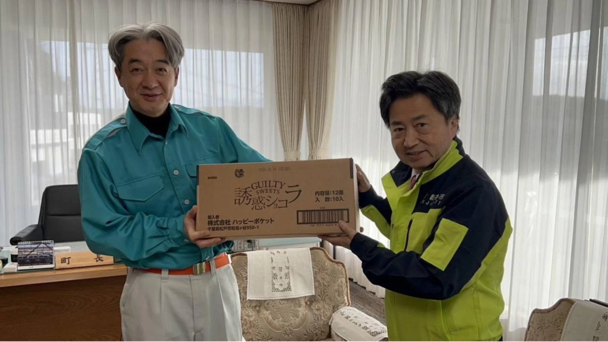 執務室で、町長服を着た男性と人吉市のジャケットを着た男性が、笑顔で「誘惑ショコラ」の箱を受け渡しています。贈り物や交流の場面のようです。