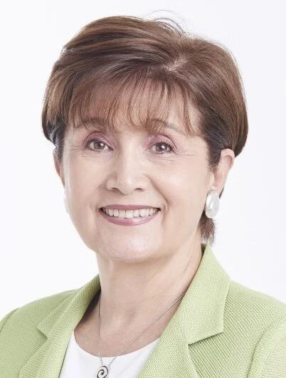 白い背景の前で、明るい緑色のジャケットを着用し、穏やかな笑顔を見せるショートヘアの女性のポートレート