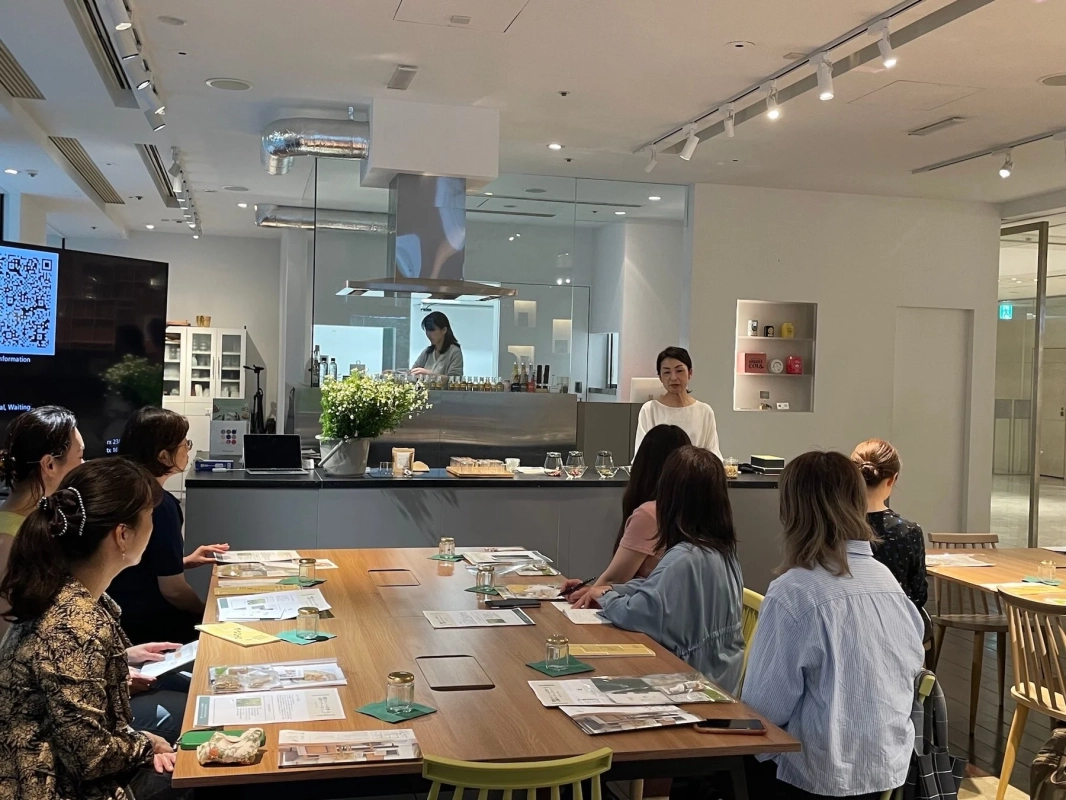 モダンなキッチンスタジオで、女性講師が参加者にプレゼンテーションを行っています。