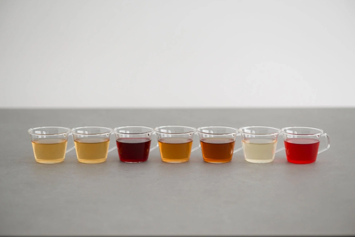 様々な色合いの液体が入った7つの小さなガラスのカップ