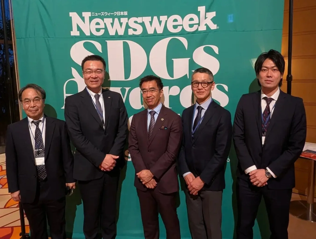 ニューズウィークSDGsアワードのイベントで、スーツ姿の男性5人が緑色のバナーを背景に並んで立っている集合写真