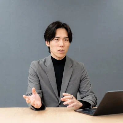 ノートパソコンの前で手を使って説明するアジア人男性