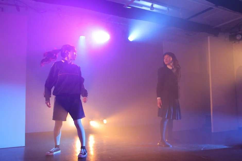 紫や青の照明が当たるステージに立つ2人の女性