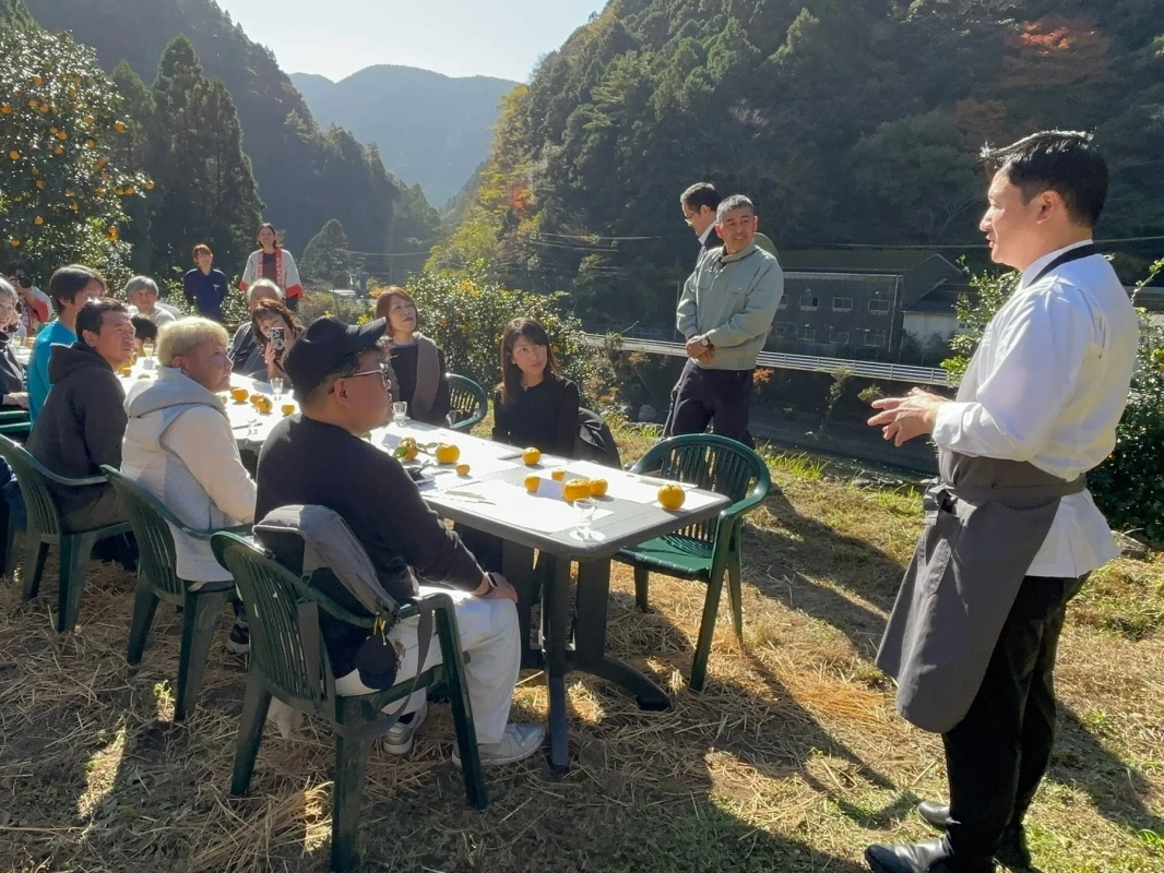 山々に囲まれた自然豊かな場所で、人々がテーブルを囲んで食事をしている様子