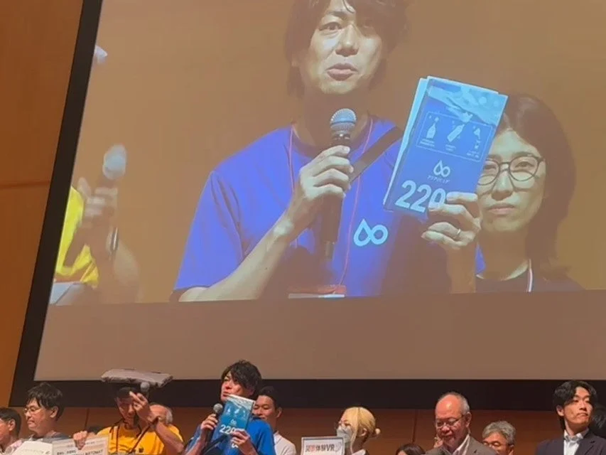 大きなスクリーンに映し出された男性がマイクを手に講演を行い、アクアポニクスに関する資料を見せている