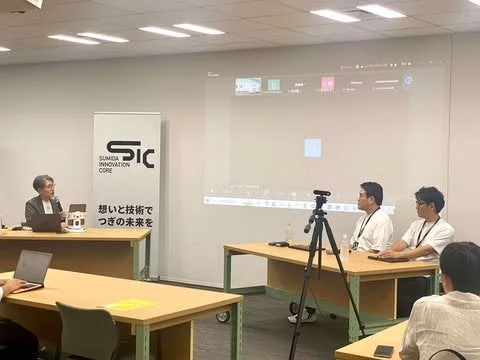 会議室でセミナーが開催されており、女性の講演者が登壇し、プロジェクターに資料が映し出されています