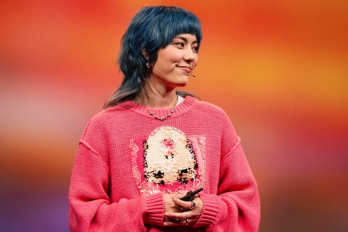 青いマレットヘアの女性が、ピンクのスパンコール付きセーターを着て微笑んでいるポートレート