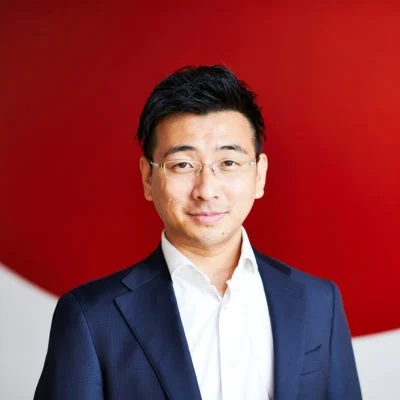 赤い背景の前でメガネをかけ、ダークスーツを着たアジア系男性のポートレート