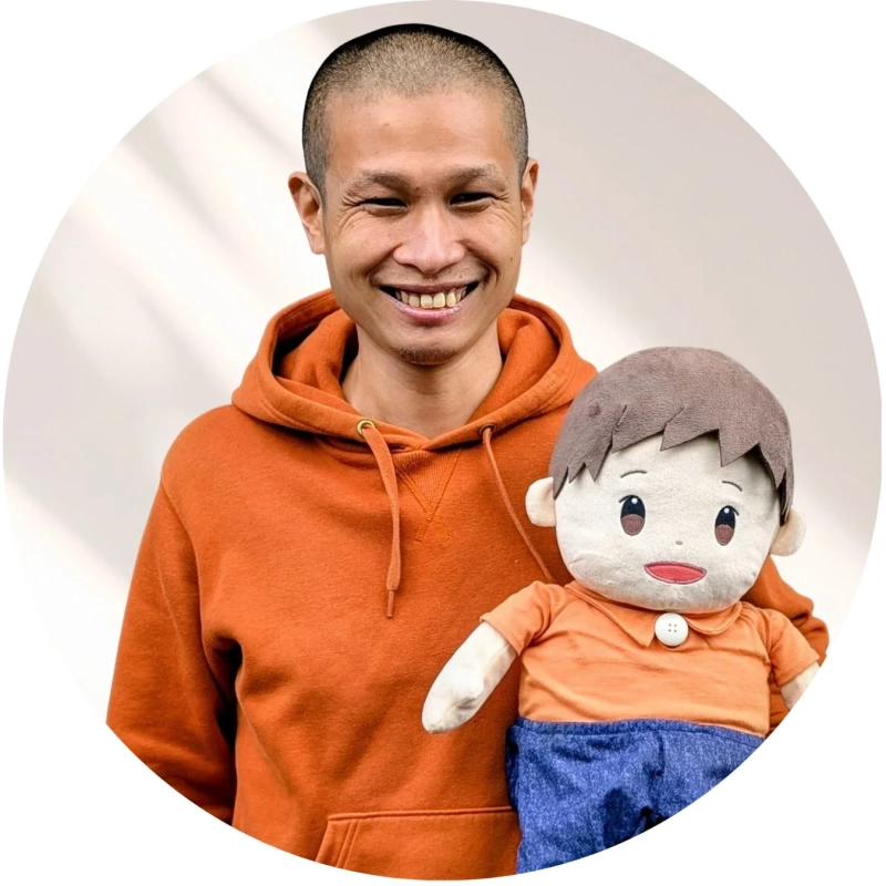 オレンジ色のパーカーを着て坊主頭の男性が、満面の笑みで男の子のぬいぐるみを持っているポートレート