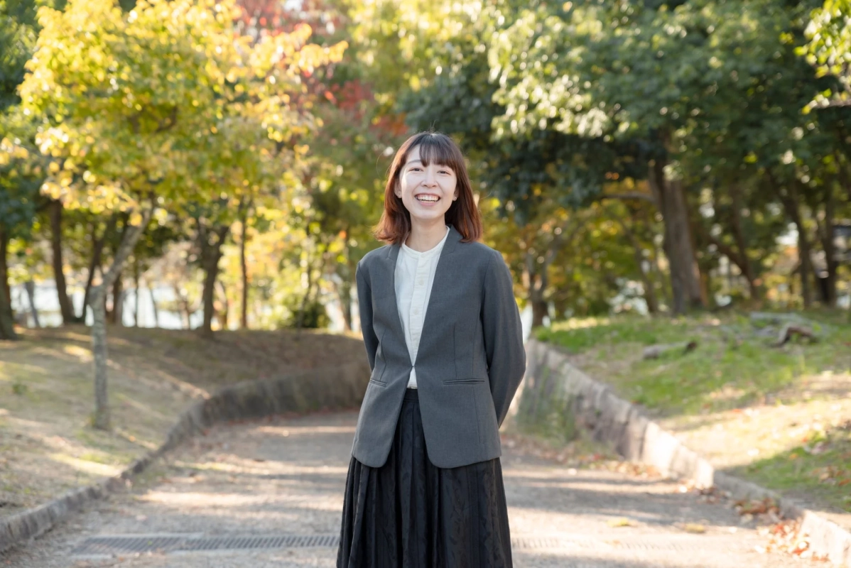 公園の小道を背景に、笑顔で立つ若い日本人女性のポートレート